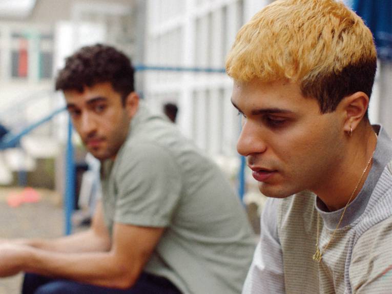 Zwei junge Männer sitzen nebeneinander vor einem Gebäude