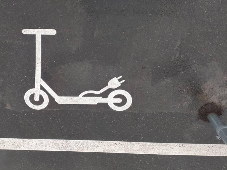 Ein auf Aspalt aufgetragenes wei&szlig;es Roller-Sybol mit einem Stromstecker, davor ein wei&szlig;er Streifen als Markierung.