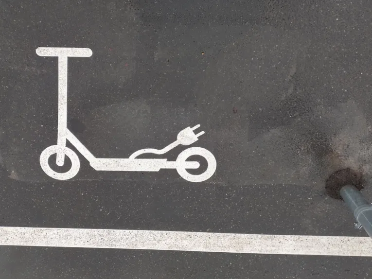 Ein auf Aspalt aufgetragenes wei&szlig;es Roller-Sybol mit einem Stromstecker, davor ein wei&szlig;er Streifen als Markierung.