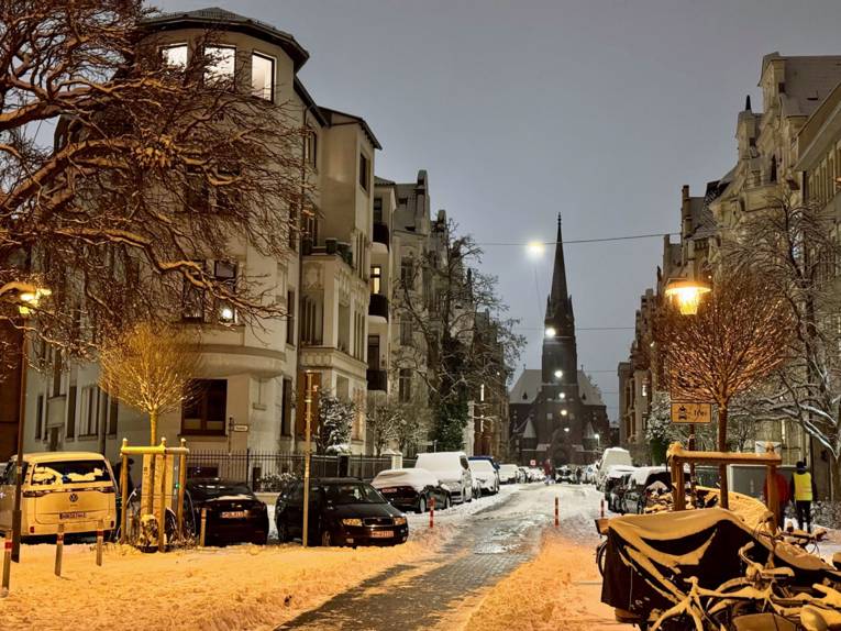 Blick in eine verschneite Großstadtstraße, an deren Ende eine Kirche steht.