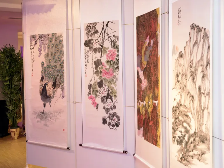 Vier Beispiele chinesischer Malerei hängen an einer Ausstellungswand, die Bilder zeigen einen Pfau, Blüten und zwei Berglandschaften.