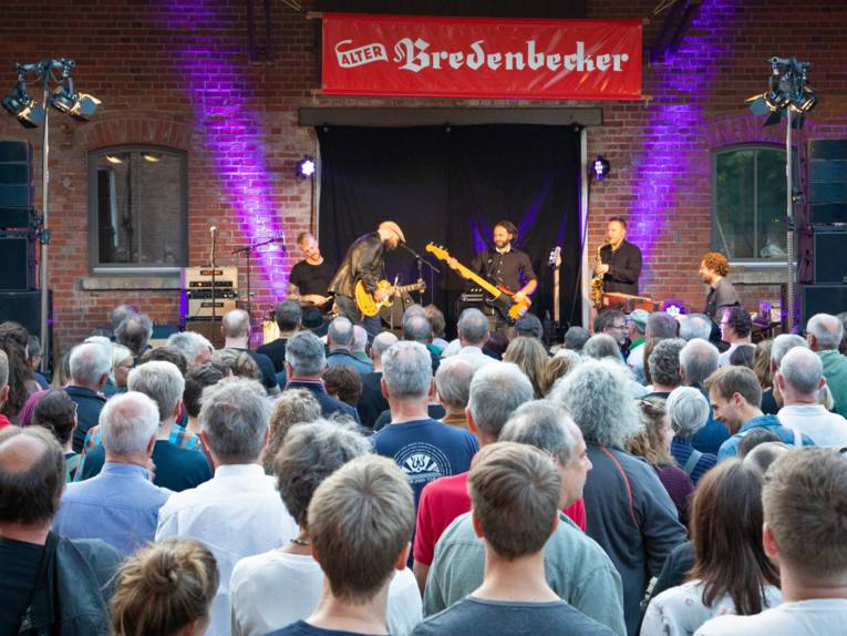 Publikum verfolgt den Auftritt einer Band auf einer Bühne im rustikalen Ambiente einer Scheune.