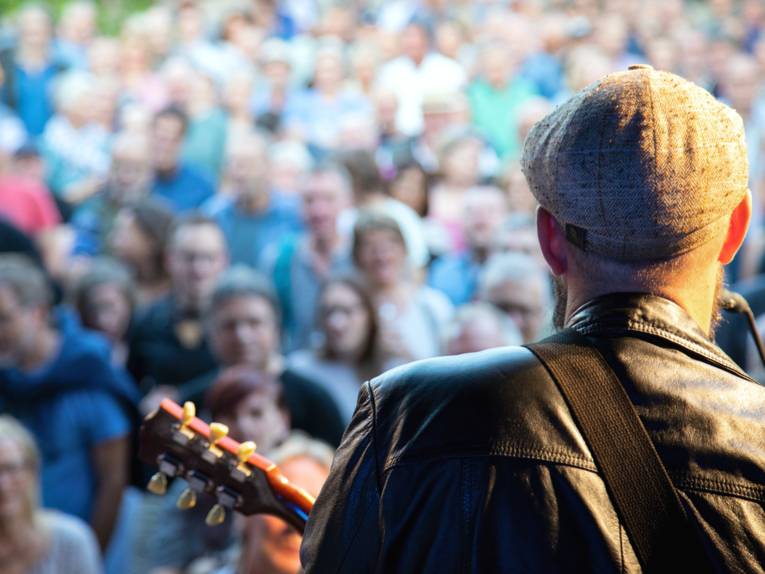 Blick von einer Bühne über die Schulter des Sängers und Gitarristen während eines Konzertes auf das Publkum.