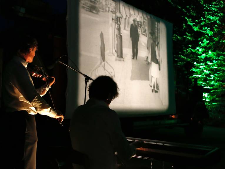 Zwei Musiker begleiten unter freiem Himmel mit ihren Instrumenten einen Stummfilm.