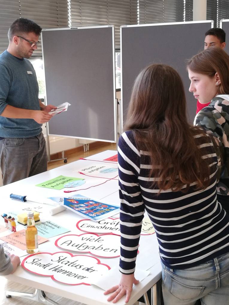 Vier junge Menschen stehen um einen Tisch mit großen beschriebenen Zetteln herum.