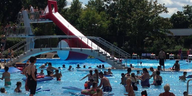 Menschen an einem Sommertag im Freibad, im Hintergrund eine große Rutsche