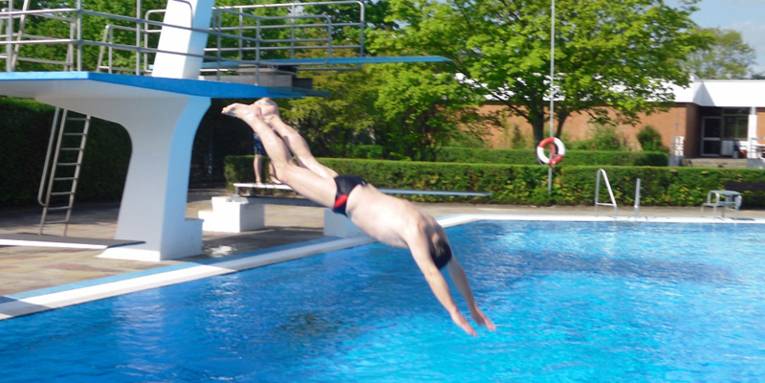 Mann der vom Sprungbrett mit einem Kopfsprung ins Schwimmbecken springt