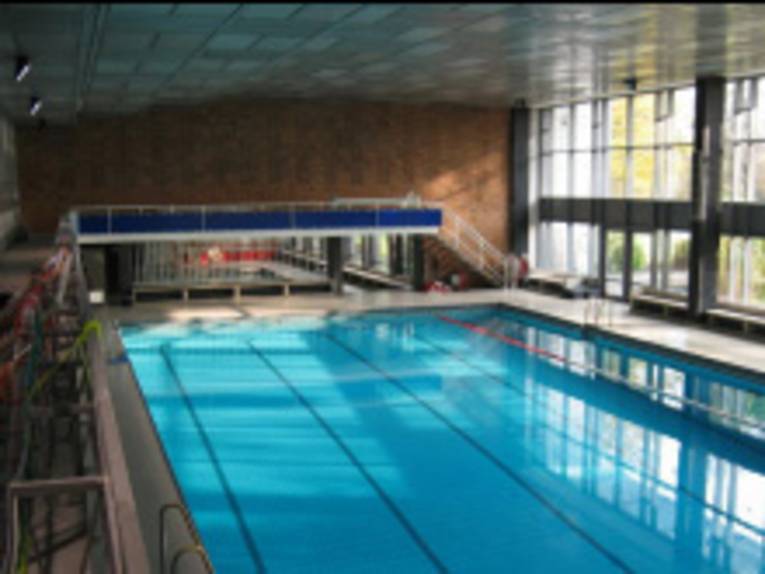 Innenraum einer Schwimmhalle: das Schwimmbecken und ein Teil der Fensterfront sind zu sehen
