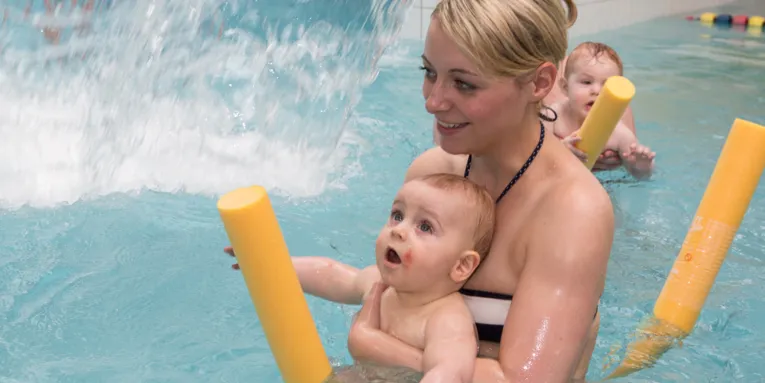Mutter mit Baby im Hallenbad im Kinderbecken auf einer Poolnoodle