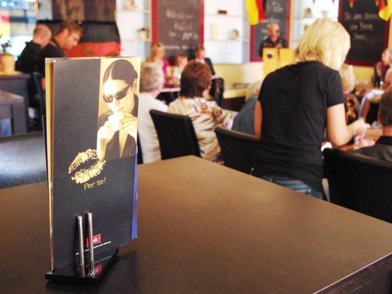 Speisekarte auf einem Tisch, im Hintergrund Gäste an Tischen