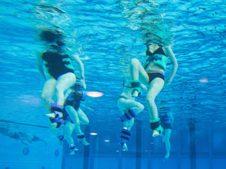 Unterwasseraufnahme von Menschen beim Aqufitnes mit Gewichtsmanschetten und Schwimmgürteln