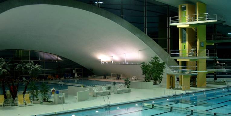 Schwimmbecken und Sprungturm eines Hallenbades am Abend