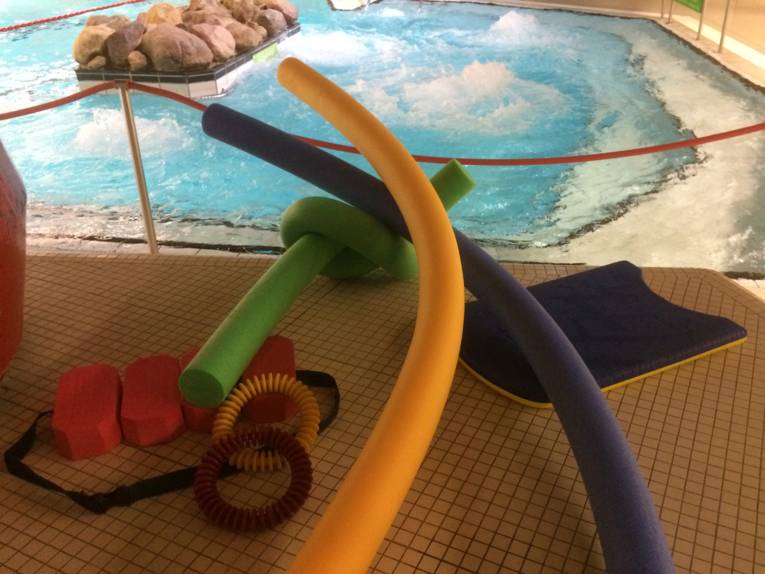 Poolnudeln, Schwimmgürtel, Tauchringe, Schwimmbrett auf gekacheltem Bodem am Rand eines Schwimmbeckens
