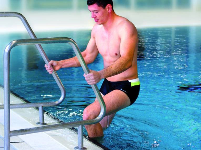 Ein junger Mann geht über eine Badeleiter in das Schwimmbecken eines Hallenbades