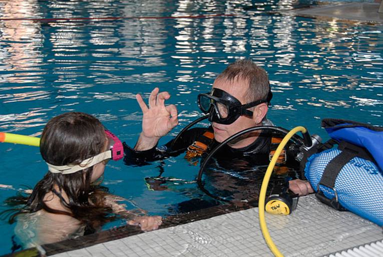 Zwei Personen mit Tauchgerät im Schwimmbad - es wird das ok-Zeichen gegeben