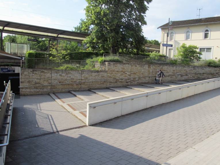 Blick auf die Ostseite des Bahnhofs in Burgdorf. Zwei Personen benutzen eine Treppe, links ist der Durchgang zur Westseite und zu den Treppen, die zu den Gleisen führen.
