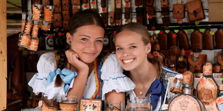 Zwei junge Frauen in Landestracht in einem Verkaufsstand aus Holz, in dem einheimische Handwerkskunst angeboten wird