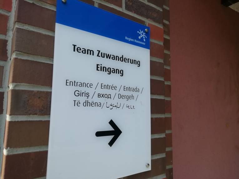 Schild an einem Eingang auf dem "Team Zuwanderung Eingang" in verschiedenen Sprachen steht