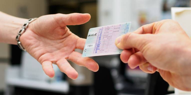 Ein Führerschein wird von einer Hand in eine andere übergeben.Änderung des Führerscheins.
