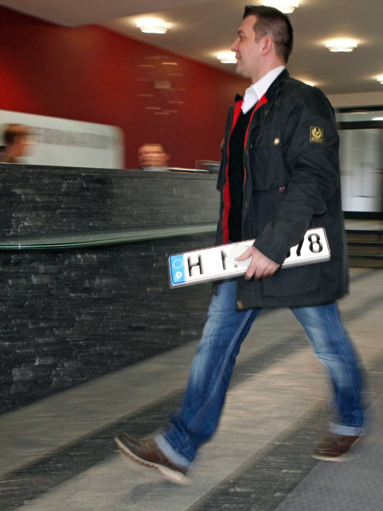 Ein Mann geht mit einem Kfz-Kennzeichen in der Hand zum Bürgerbüro der Region Hannover im Regionshaus an der Hildesheimer Straße in Hannover.