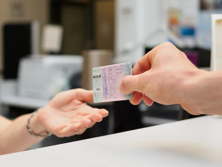 Eine Hand übergibt einen Führerschein in eine andere Hand