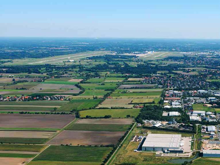 Blick über eine große Flächen mit grünen Flächen, Feldern und Industriegebieten.