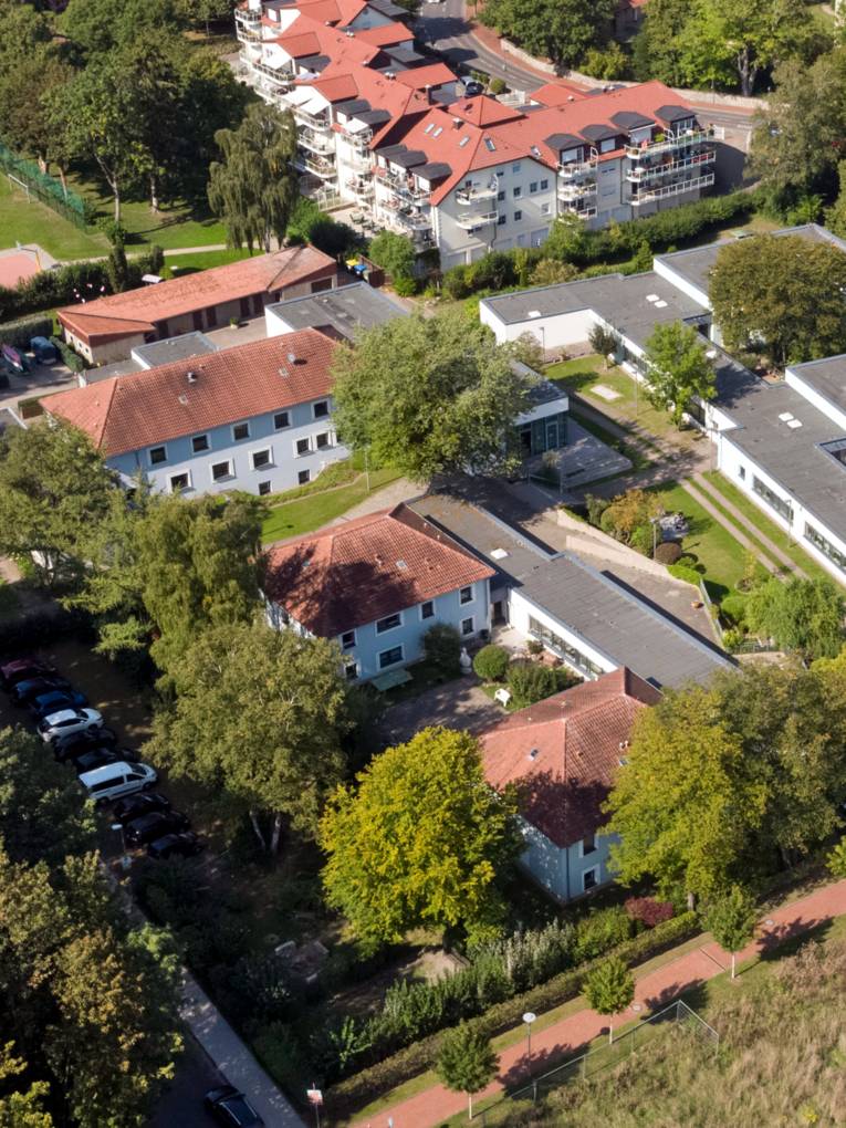 Luftaufnahme eines Gebäudekomplexes, auf dem Außengelände sind Spiel- und Sportgeräte.