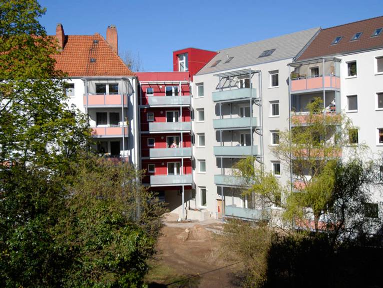 Mehrgeschossige weisse Wohnhäuser mit farbigen Balkons, im Vordergrund Bäume