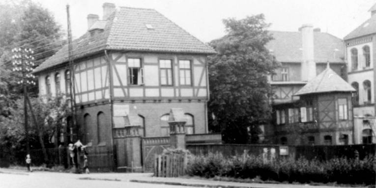 Schwarz-Weiß-Foto: Hinter einem gemauerten Eingangstor steht ein Ensemble mehrerer mehrgeschossiger Fachwerkhäuser.