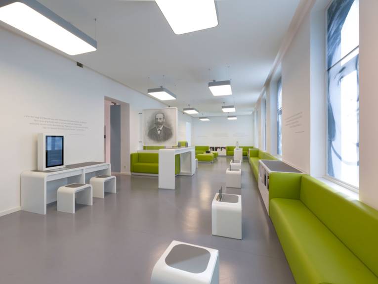 Ein Raum mit mehreren Sitzgelegenheiten, kleinen Medientischen und Regalen mit Büchern bzw. Infomaterial.