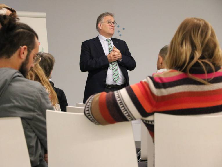 Ein Mann im Anzug steht vor sitzenden Menschen und redet.