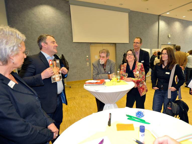 Gruppe von Personen um zwei Stehtische herum stehend