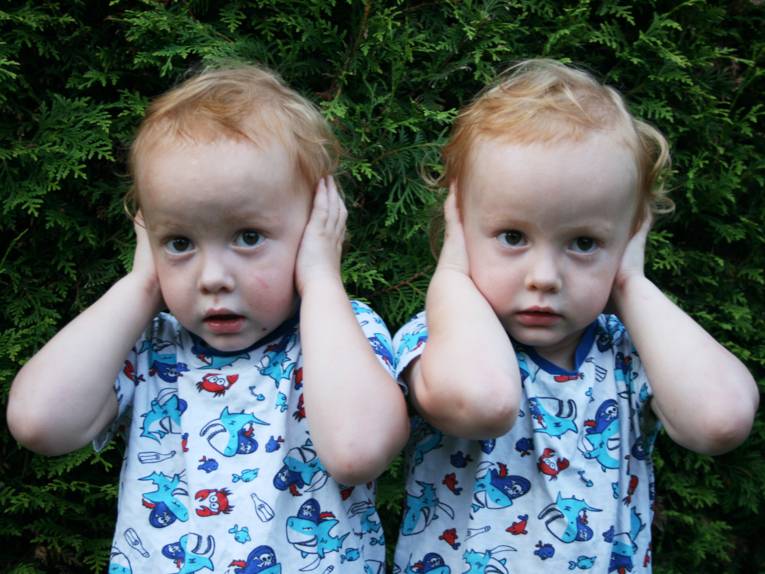 Zwei Kleinkinder im Porträt, beide gucken traurig und halten sich die Ohren zu.