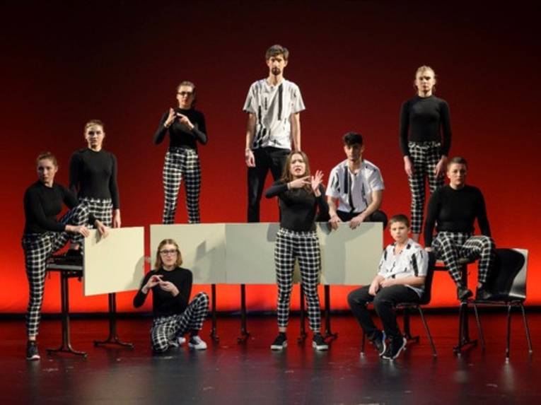 Junge Menschen auf einer Bühne vor einem rot beleuchteten Hintergrund