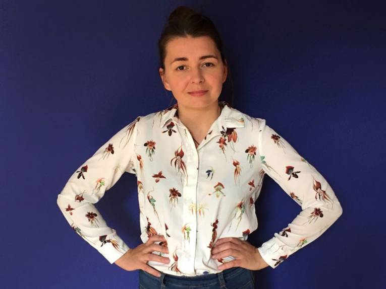 Eine Frau hat ihre Hände in die Hüfte gestemmt. Sie trägt eine Bluse.