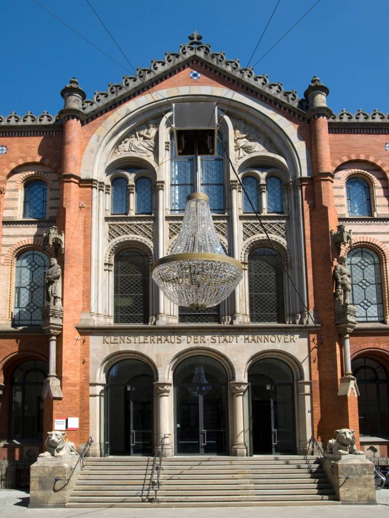 Zu sehen sind ein großer Kronleuchter in der Mitte der Straße und der Eingang zum Künstlerhaus.