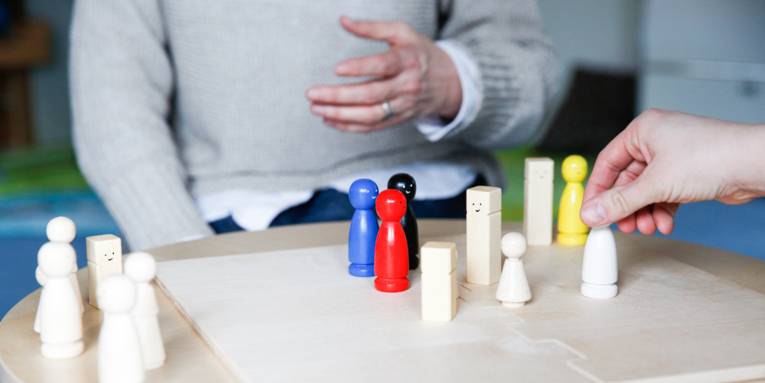 Ein Brettspiel mit verschiedenfarbigen Holzfiguren auf einem runden Tisch, eine Hand bewegt eine Holzfigur.