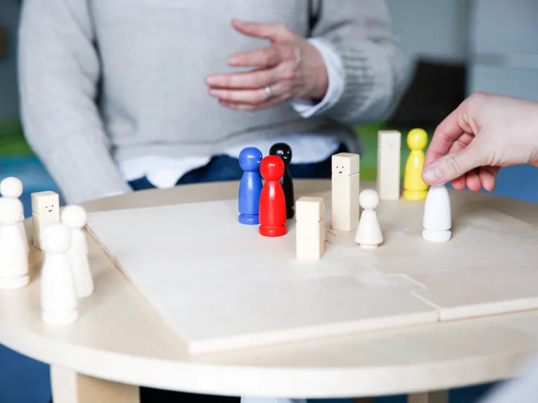 Ein Brettspiel mit verschiedenfarbigen Holzfiguren auf einem runden Tisch, eine Hand bewegt eine Holzfigur.