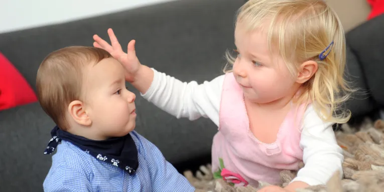Zwei kleine Kinder auf einem Teppich beim Spielen 