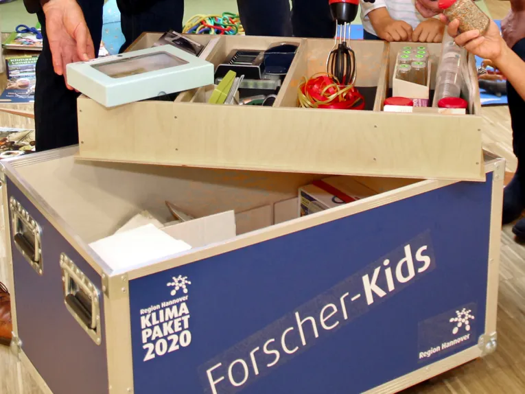 Hände nehmen Materialien zum Forschen und Entdecken aus einer Entdeckerkiste