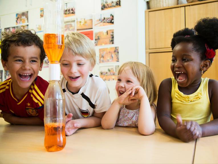 Forschen: Zwei Jungen und zwei Mädchen beobachten ein Experiment mit einer Flasche und Flüssigkeiten.