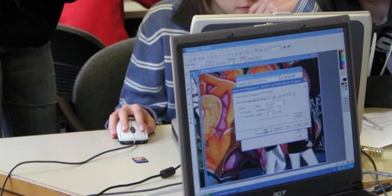 Blick auf einen eingeschaltete Computermonitor und Personen im Raum.