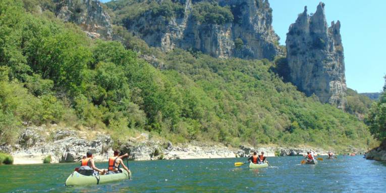 Jugendliche fahren mit Kanus an einem Flussufer entlang.