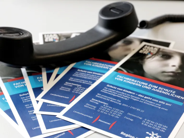 Mehrere Exemplare eines Flyers liegen aufgefächert auf einem Tisch. darauf liegt der Hörer eines Telefons.