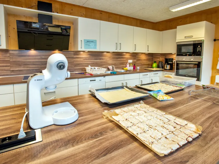K&uuml;che mit Arbeitsfl&auml;che und K&uuml;chenmaschine, Speisen liegen auf Backblechen.