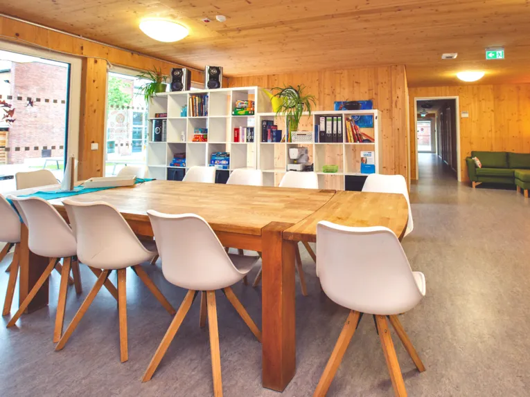 Esszimmer mit Esstisch, St&uuml;hlen und einer Medienwand im Hintergrund.