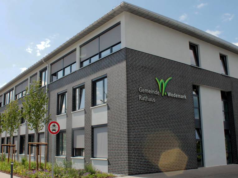 Modernes Gebäude mit Schrägdach, an der Seite steht "Gemeinde Wedemark Rathaus" mit einem stilisierten, grünen "W"
