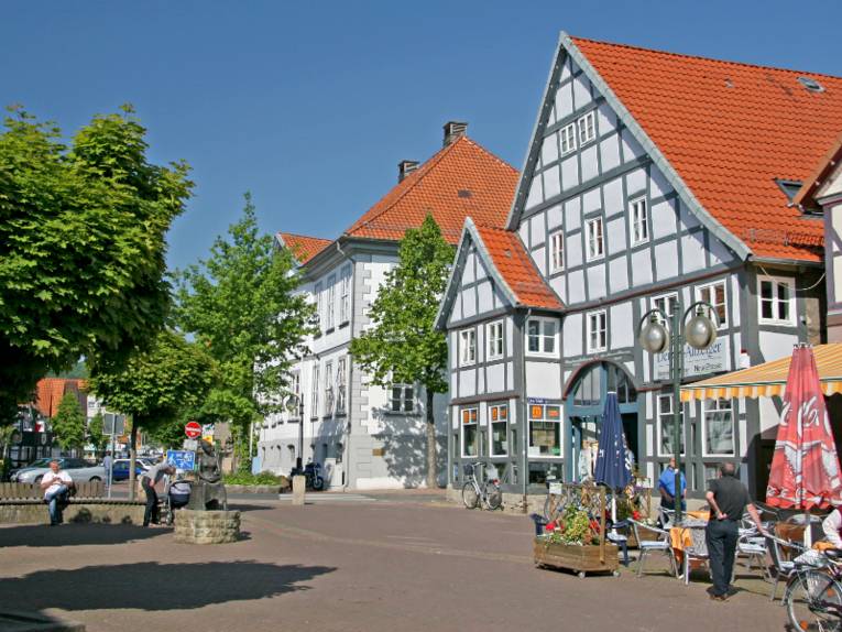 Fachwerkhäuser vor dunkelblauem Himmel. Auf der linken Seite ist bildet eine gepflasterte Freifläche einen Platz, hier wachsen auch Bäume.