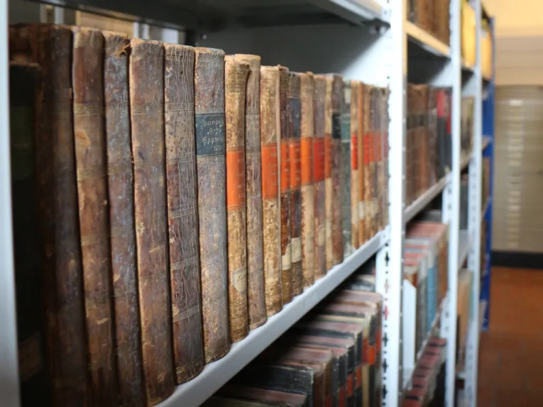 Ein Regal mit sehr alten Büchern links im Bild.