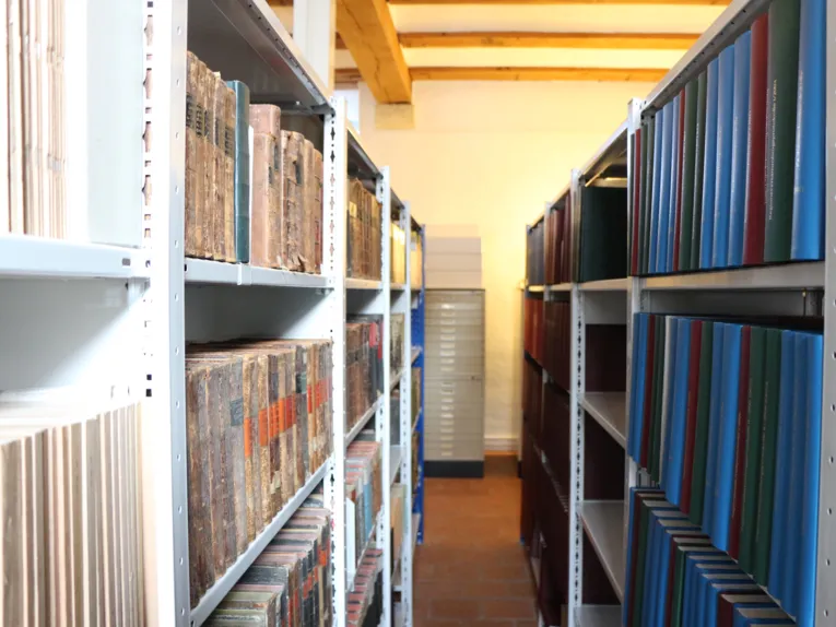 Zwei Regalreihen mit Büchern und Ordner und dazwischen ein Durchgang.
